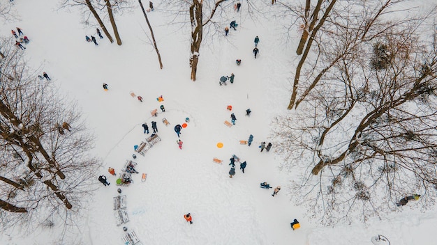 Niños felices deslizándose por la colina nevada en el parque de la ciudad vista aérea