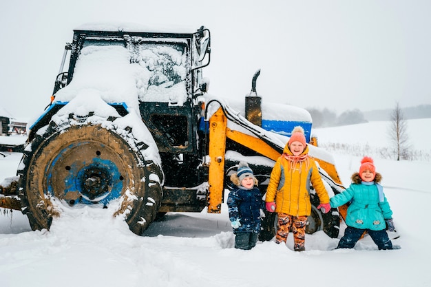 Niños felices frente a un tractor en un día de invierno al aire libre