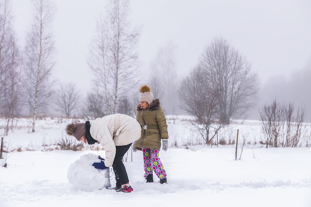 Los niños felices hacen un muñeco de nieve en un campo cubierto de nieve en el campo.