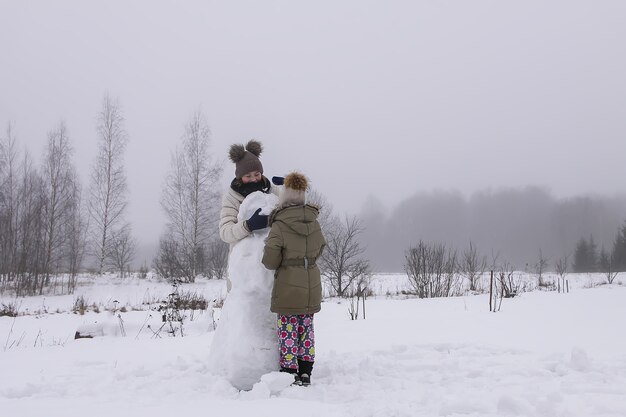 Los niños felices hacen un muñeco de nieve en un campo cubierto de nieve en el campo.