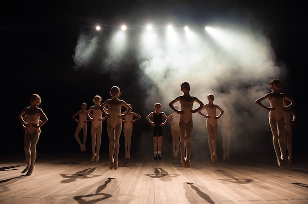 Niños felices haciendo ballet saltan en una escena oscura iluminada.