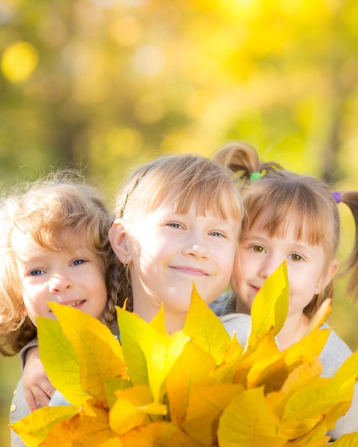 Niños felices con hojas de arce en el parque de otoño