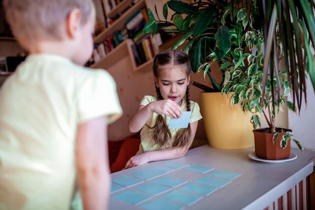 Niños felices jugando al memo del juego de mesa en el interior doméstico, los valores familiares en realidad