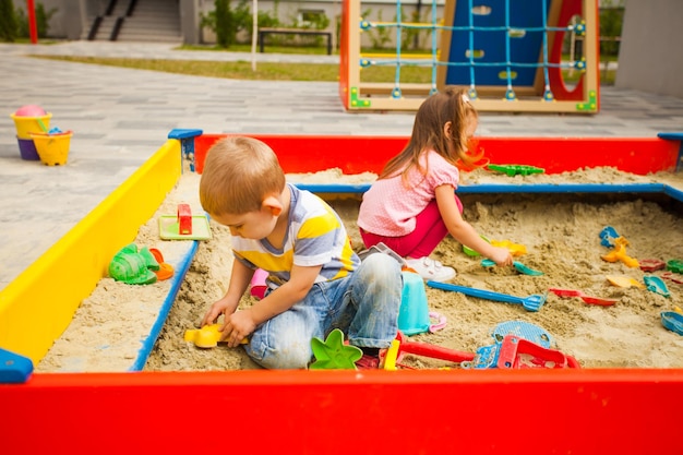 Niños felices jugando con arena en el patio de recreo. Actividades creativas al aire libre para niños.