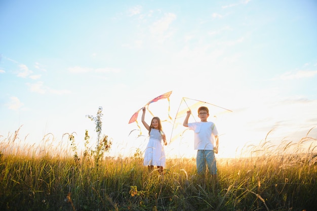 Niños felices lanzan una cometa en el campo al atardecer Niño y niña en vacaciones de verano