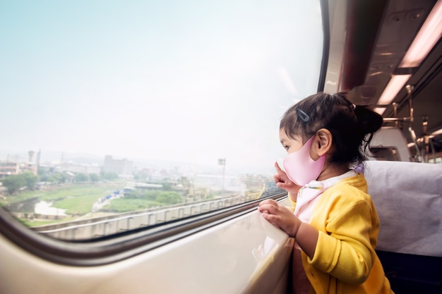 Niños felices con máscara de protección quirúrgica en un tren