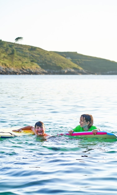 Niños felices mirando a cámara jugando en el mar con bodyboard. Niños divirtiéndose al aire libre. Concepto de vacaciones de verano y estilo de vida saludable.