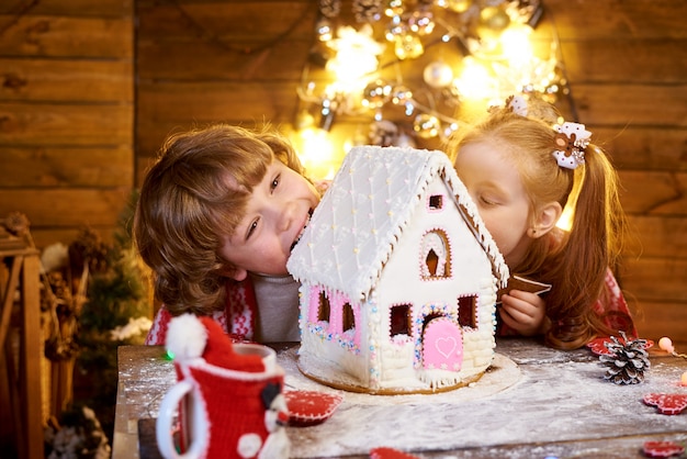 Niños felices muerden pan de jengibre de Navidad en una habitación decorada para las vacaciones.