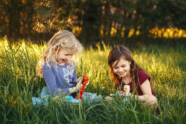 Niños felices, niñas jugando con muñecas en el parque, niños sentados en la hierba en el prado jugando a los juguetes.