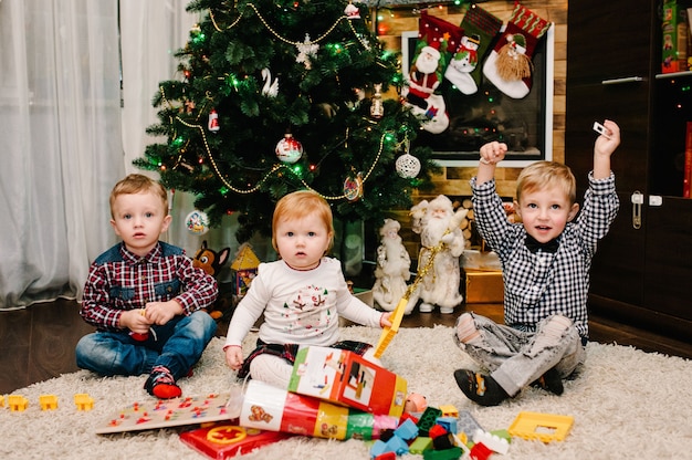 Niños felices, niños, hija e hijo, niño y niña desempaquetan regalos cerca del árbol de navidad y la chimenea.