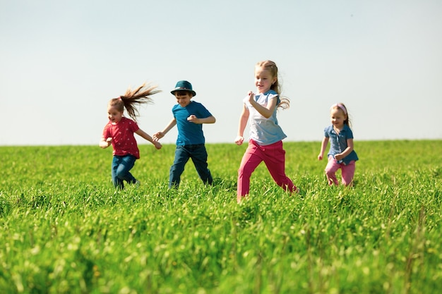 Niños felices de niños y niñas corren en el parque sobre la hierba en un día soleado de verano