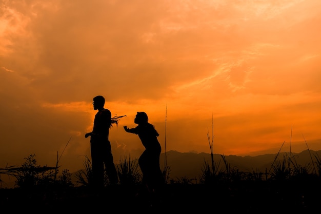 niños felices de la pareja jugando en el prado al atardecer, silueta