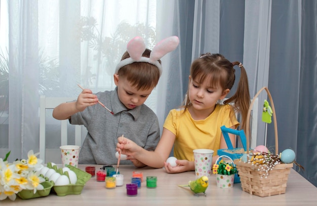 Niños felices de Pascua pintan y dibujan huevos de Pascua Niños encantadores preparándose para las vacaciones Linda niña y niño decoran huevos de Pascua