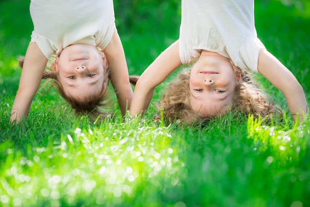 Niños felices de pie boca abajo sobre la hierba verde Niños sonrientes divirtiéndose en el parque de primavera Concepto de estilo de vida saludable