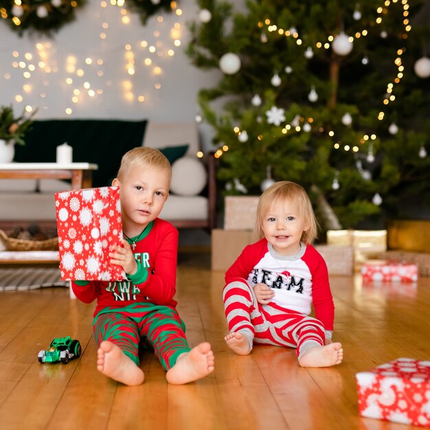 Niños felices en pijama jugando con regalos de Navidad