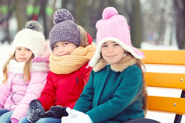 Foto niños felices sentados en un banco de madera al aire libre en invierno