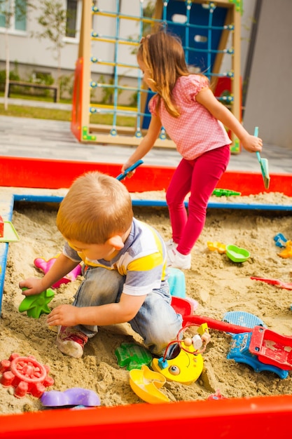 Foto niños felices sentados en una caja de arena jugando con juguetes de plástico de colores.
