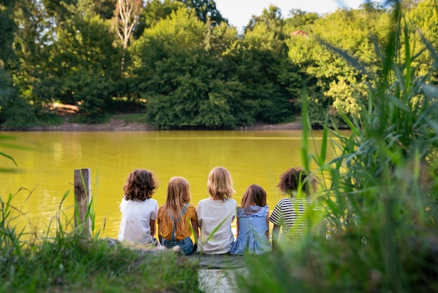 Niños felices sentados junto al lago vista trasera