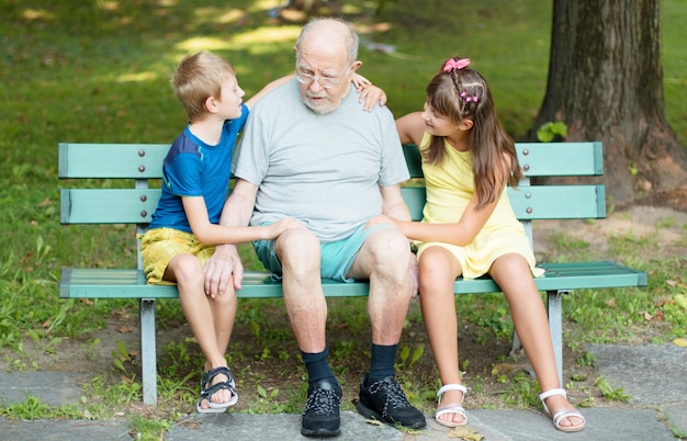 Niños felices y su abuelo están jugando juntos en el banco del parque