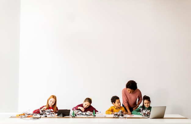 Niños felices con su maestra de ciencias afroamericana con computadora portátil programando juguetes eléctricos y robots en la clase de robótica