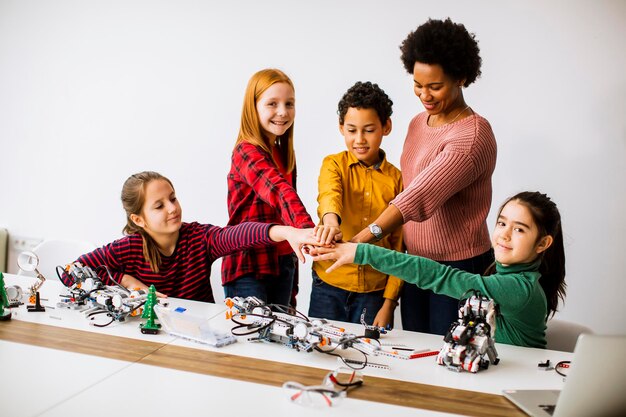 Niños felices con su maestra de ciencias afroamericana programando juguetes eléctricos y robots en la clase de robótica