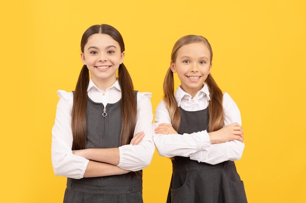 Niños felices usan uniforme escolar con los brazos cruzados fondo amarillo 1 de septiembre