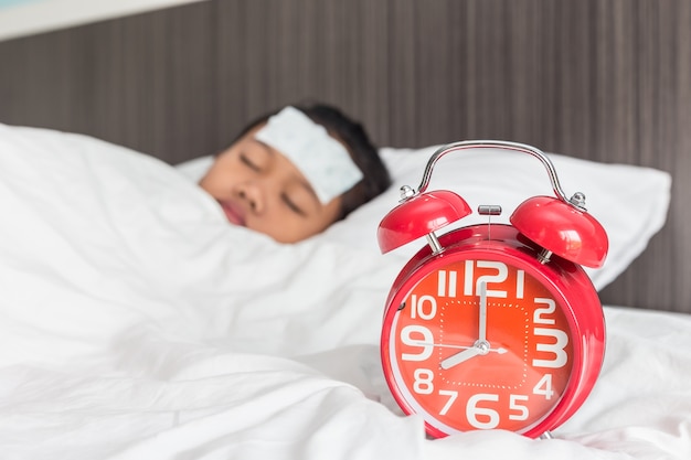 Niños con fiebre blanca y fría en la frente y durmiendo en la cama, se centran en el reloj rojo