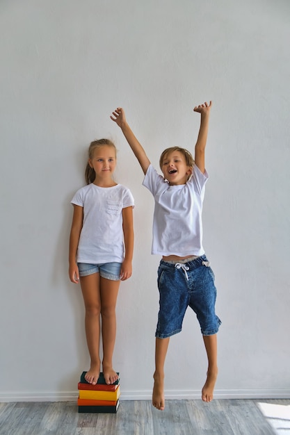 Niños geniales, niño y niña miden su altura y comparan, diviértase cerca de la pared blanca