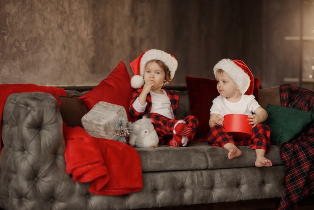 Niños con gorro de Papá Noel en una gran silla acogedora en la sala de estar