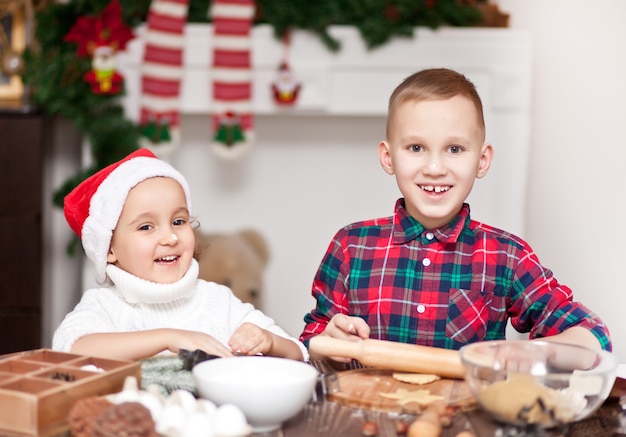 Niños con gorro de Papá Noel para hornear galletas de Navidad en casa.