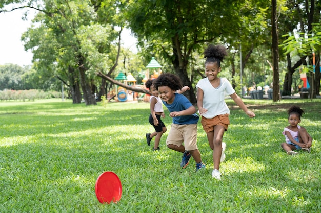 Los niños del grupo, las niñas y los niños afroamericanos, se divierten jugando y lanzando discos voladores rojos en el parque