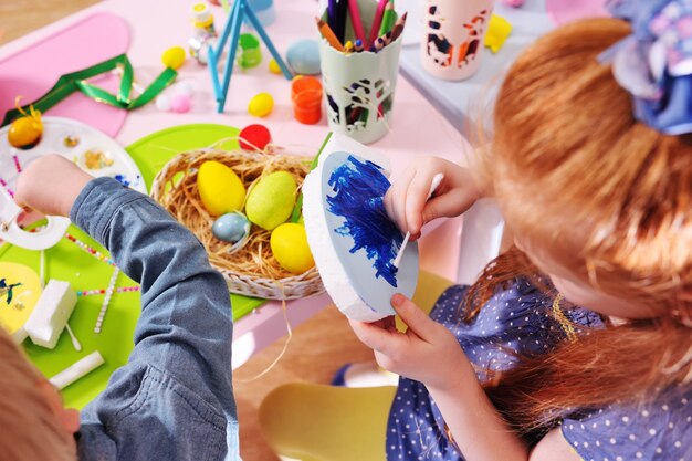 Los niños en la guardería pintan los huevos para la canasta de Pascua en la mesa.