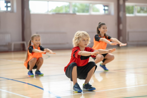 niños haciendo ejercicio en el gimnasio y haciendo sentadillas.