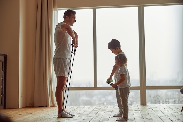 Niños haciendo ejercicio con padre atlético en casa