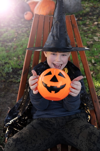 Niños de Halloween. Niño lindo, niño con sombrero de bruja con cubo de caramelo naranja Jack O Lantern. Feliz Halloween.