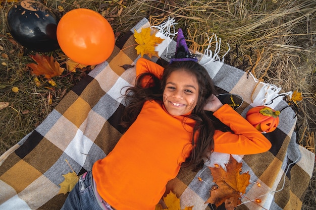 Niños de Halloween. Retrato de niña sonriente con cabello castaño tendido sobre una manta. Niños divertidos con disfraces de carnaval.