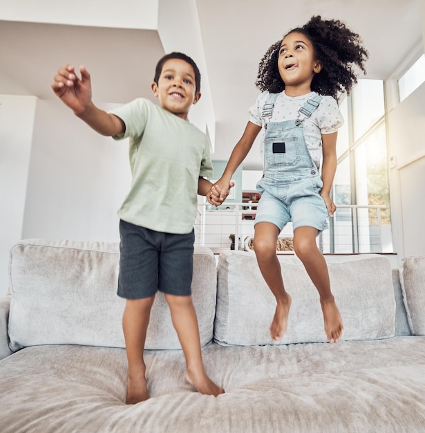 Los niños, hermano y hermana, se unen y saltan en el sofá de la casa o en la sala de estar del hotel en juegos divertidos y juegos de energía.