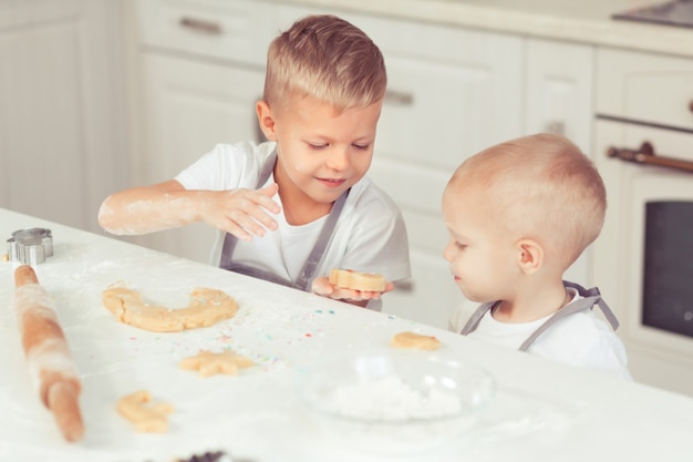 Los niños de los hermanos divertidos de la familia feliz están preparando la masa y hornear galletas en la cocina