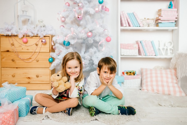 Niños hermosos y divertidos posando para la cámara en una habitación con decoraciones de vacaciones de año nuevo.