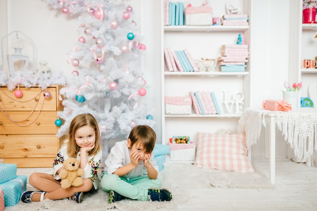 Niños hermosos y divertidos posando para la cámara en una habitación infantil con decoraciones de vacaciones de invierno.