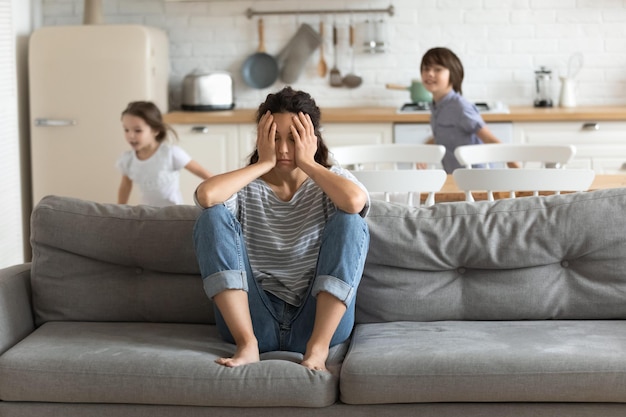 Foto niños hiperactivos cansados y corriendo cerca de una madre molesta sentada en el sofá mamá frustrante estresante siente pesadez y dolor de cabeza en casa el padre fatigado no quiere jugar con su hijo y su hija