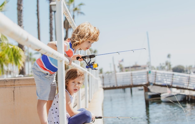 Niños hobby par de niños pescando en el muelle niño en el embarcadero con varilla niño y niña con varilla de pesca