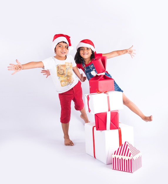 Niños indios celebrando la Navidad con regalos, árbol y sombrero rojo de Santa Claus, aislado sobre fondo blanco.
