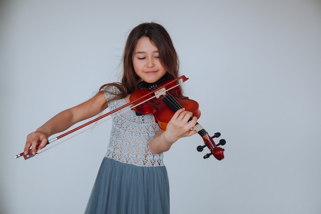 Los niños y los instrumentos musicales Niña morena con un hermoso vestido tocando el violín en el interior