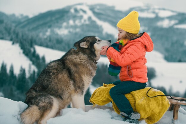 Niños de invierno con perro husky en la nieve husky siberiano con ojos azules en el bosque de invierno austria o