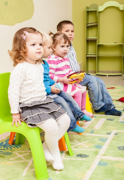Foto niños en el jardín de infantes sentados en las sillas y escuchar algo.