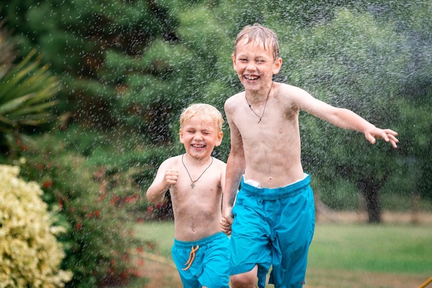 Los niños juegan con agua en un caluroso día de verano Niños con aspersores de jardín Diversión al aire libre Los niños corren en un campo bajo gotas de agua