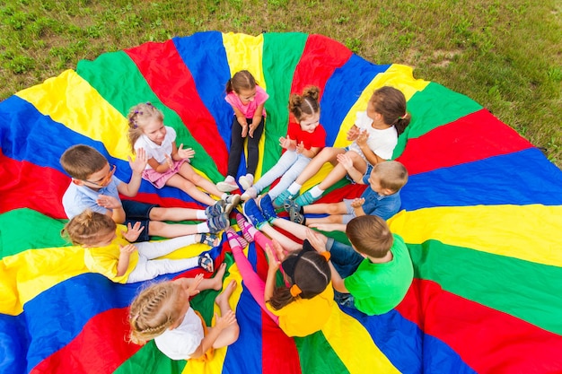 Foto los niños juegan al aire libre, sentados en el arco iris parashute, aplauden