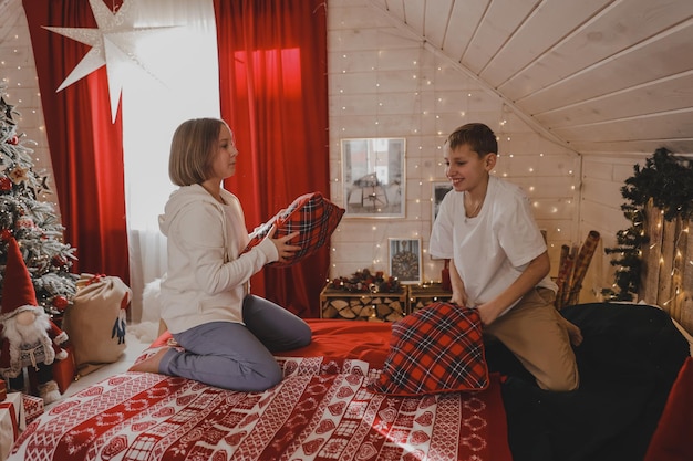 Los niños juegan con almohadas en la cama en el dormitorio decorado con Navidad, peleas de almohadas, el concepto de las vacaciones de Año Nuevo