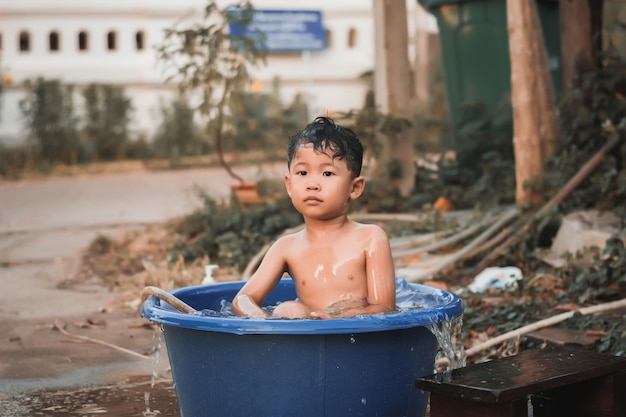 Los niños juegan y bañan agua en el jardín, sentados en un balde de agua.